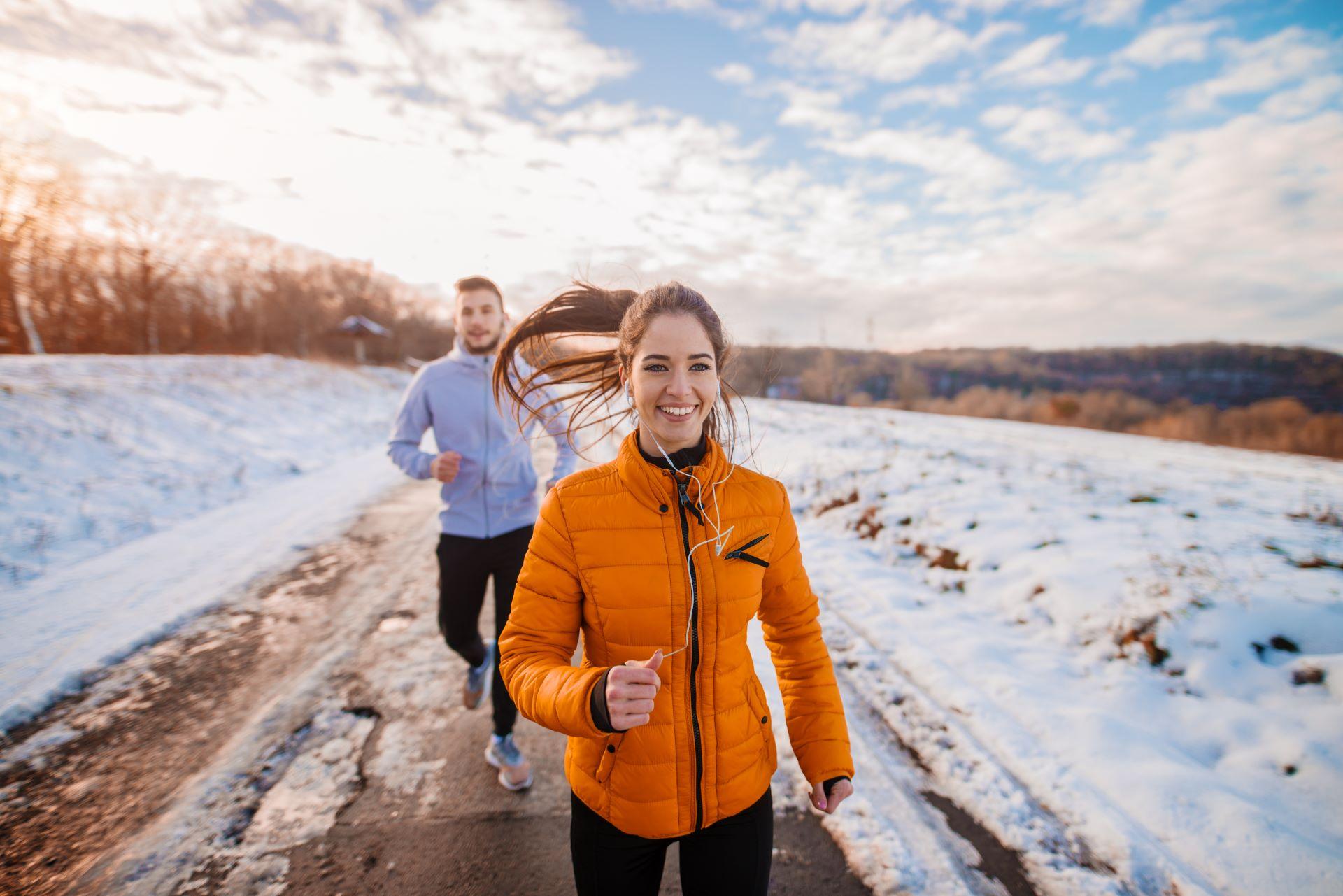 Zwei Personen joggen bei Sonnenuntergang im Schnee.